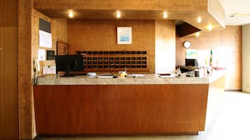 Una recepción con mostrador de madera, una computadora y un tablón de anuncios con avisos varios.