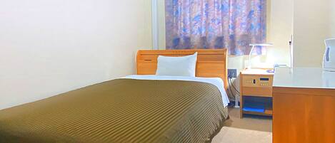 Una habitación de hotel con cama, escritorio, lámpara y ventana con cortinas.