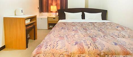 A hotel room with a bed, a desk, a nightstand, and a lamp.