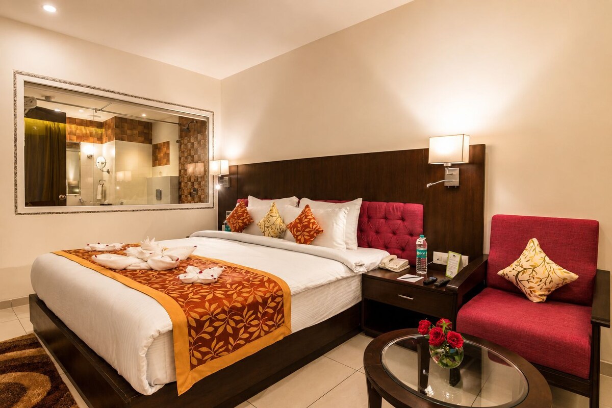 Une chambre d’hôtel avec un grand lit, une table de chevet, une chaise, une table ronde en verre et un miroir.