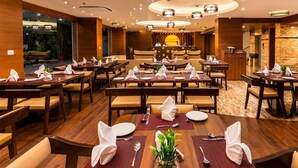 Een restaurantgedeelte in een hotel met meerdere gedekte tafels, een centrale zithoek en uitzicht op het buitengebeuren.