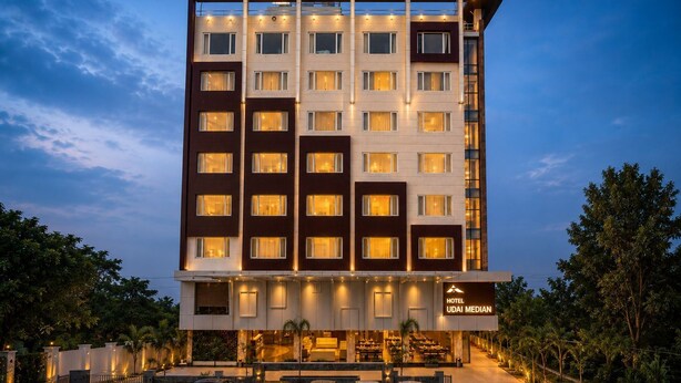 Een hotel met meerdere verdiepingen, met een modern ontwerp, een opvallende ingang met een overdekt gedeelte en een zichtbaar bord waarop de naam 'UDAI MEDIAN' staat.