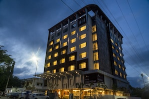 Un hotel de varios pisos con ventanas iluminadas, un área de entrada cubierta y un cartel que indica que es el "Hotel Udal Median".