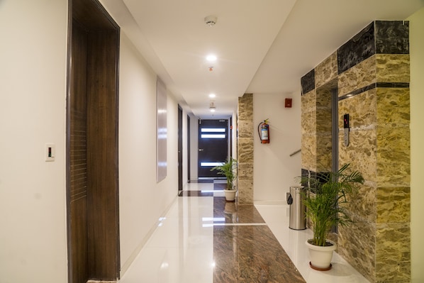 Un pasillo moderno con suelo de mármol, una planta en maceta y un extintor en la pared.