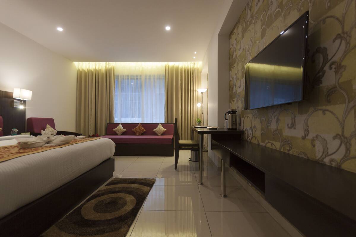 Ein Hotelzimmer mit einem Bett, einem Sofa, einem Schreibtisch und einem an der Wand befestigten Fernseher.
