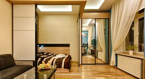 A modern hotel room with a bed, a glass table with fruits, a sofa, and a view into the adjacent room. - Apartamenty Galicja (Kraków)