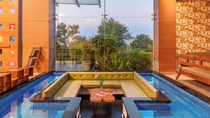 Un espace piscine intérieur moderne doté d’un toit en verre, d’un coin salon et d’une vue sur l’extérieur.
