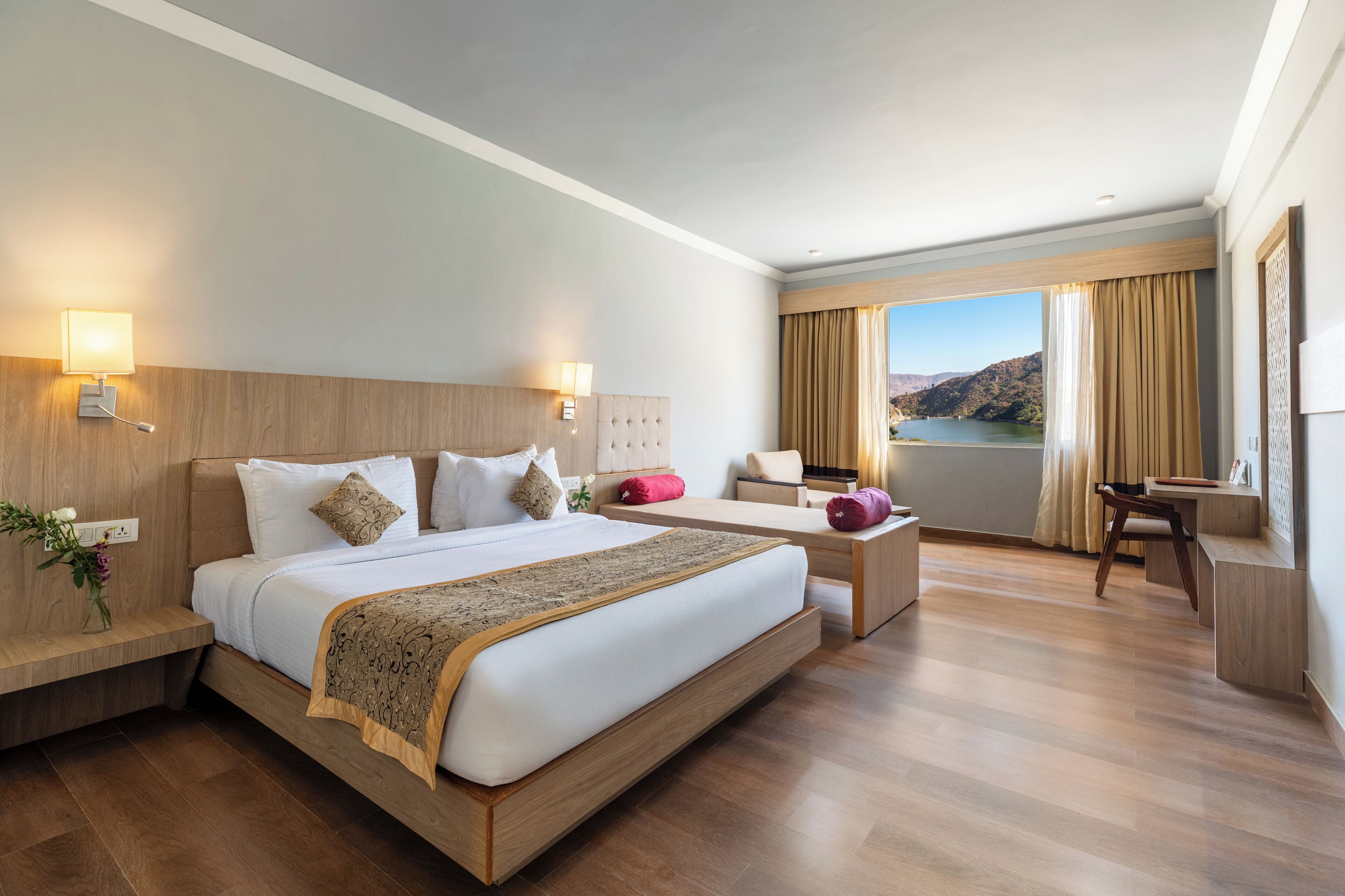 A modern hotel room with a large bed, bedside tables, a desk, and a view of a lake.
