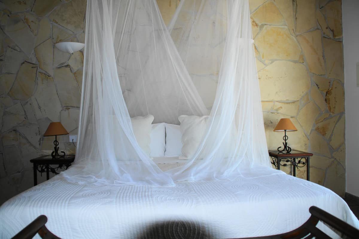 Una cama con dosel, dos mesitas de noche con lámparas y una pared de piedra.