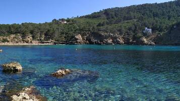 A coastal area with clear turquoise water, rocky shorelines, and a hillside with buildings.