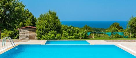 Una piscina azul cristalina con un trampolín, rodeada de exuberante vegetación y vistas al océano.