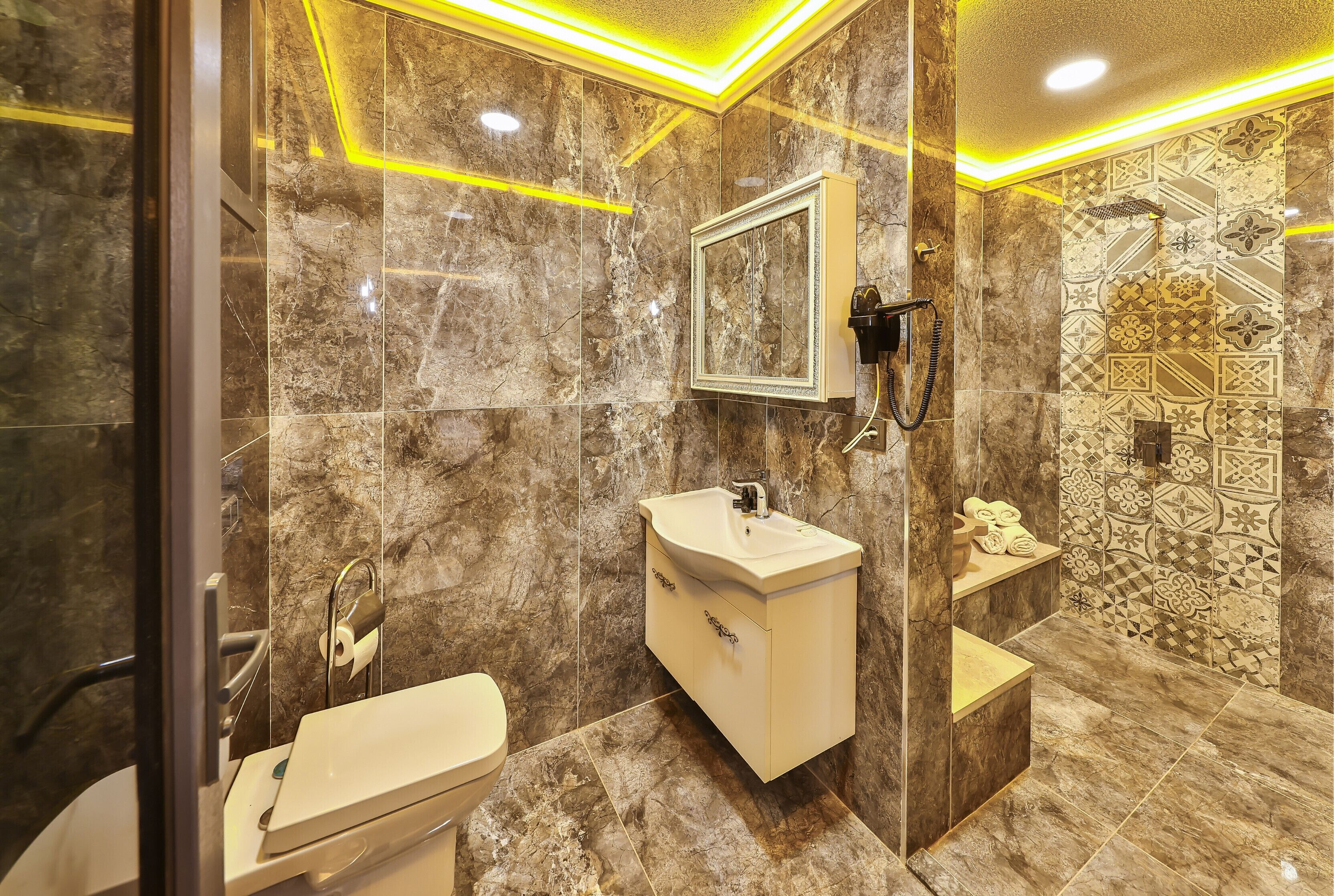 Un baño moderno con lavamanos de mármol, cabina de ducha con paneles de vidrio y azulejos estampados.