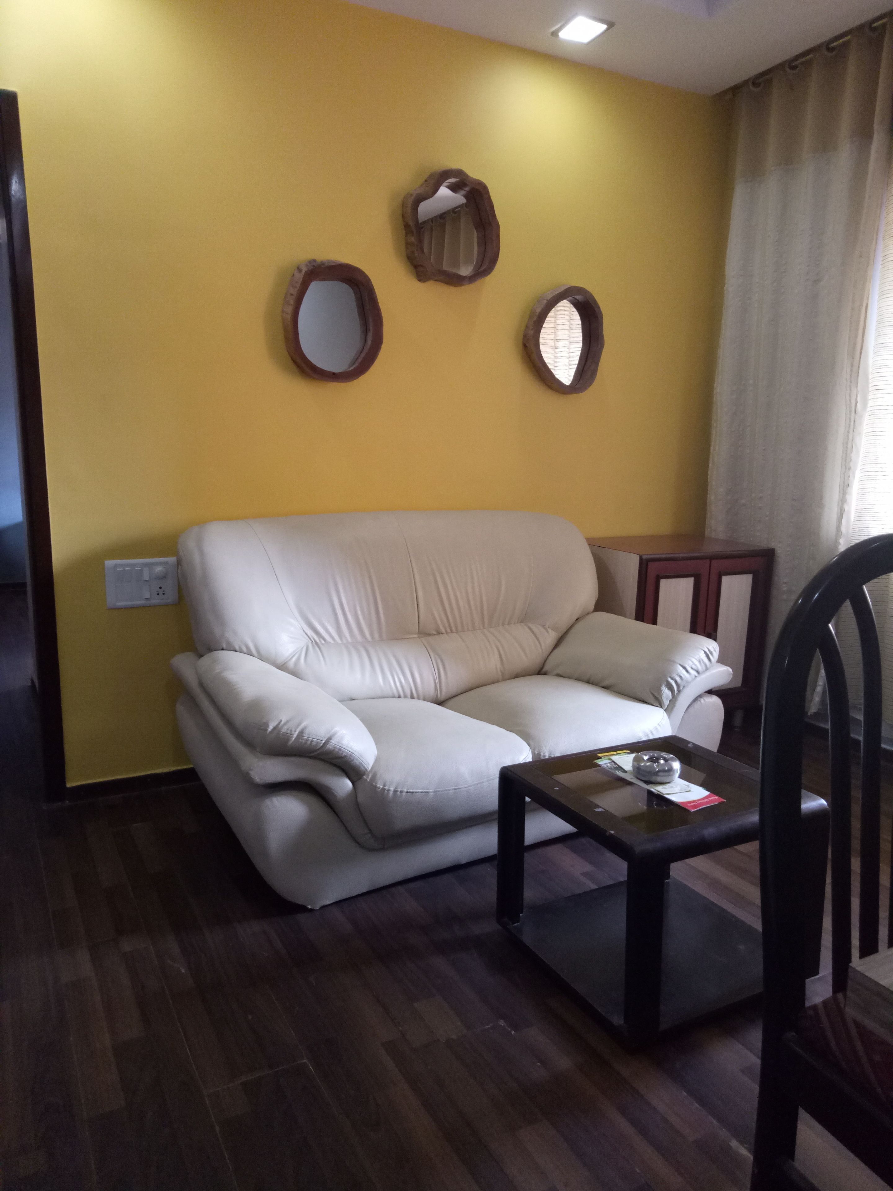 Una sala de estar con un sofá color crema, una mesita y dos espejos colgados en la pared.