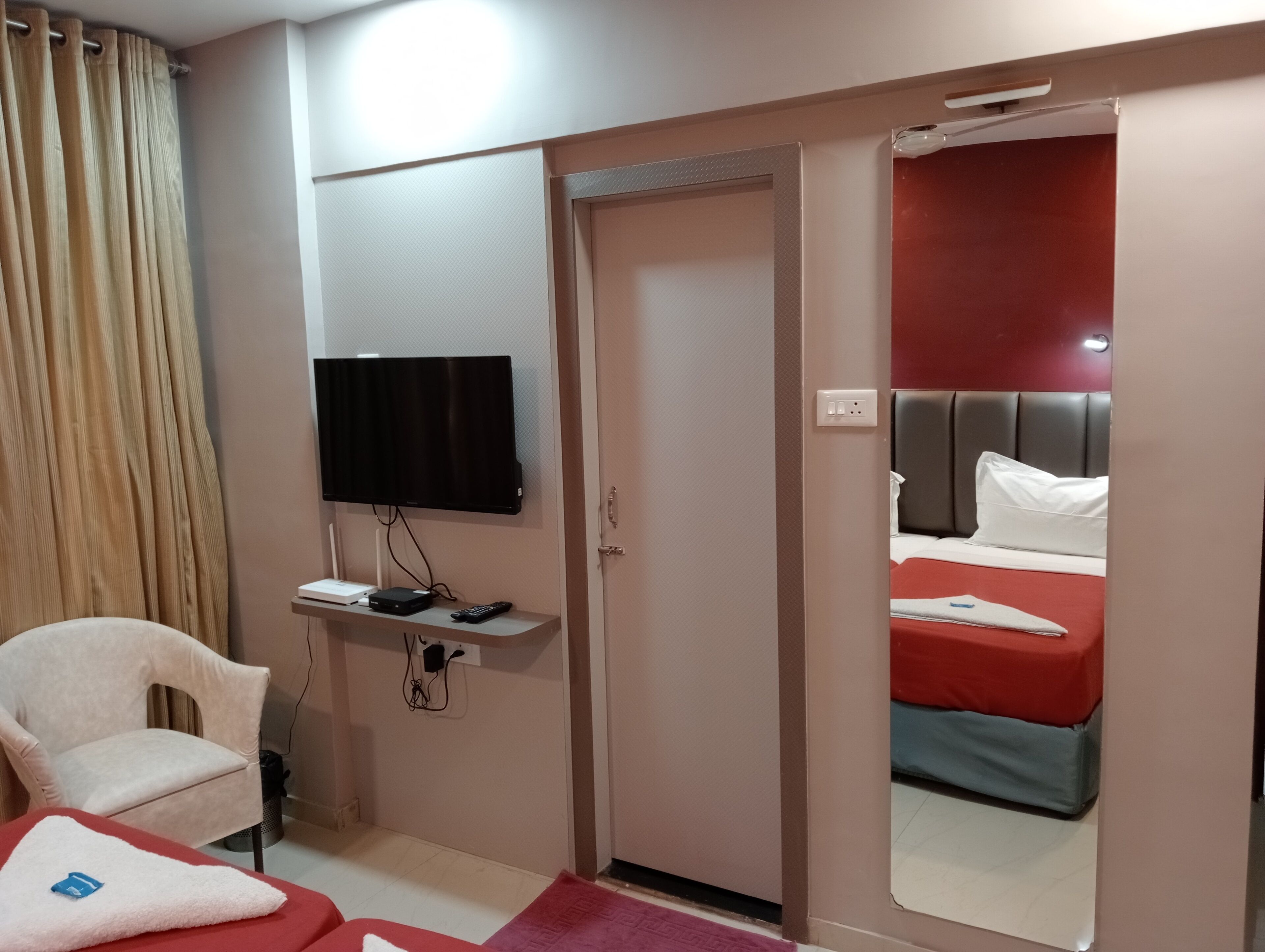 A hotel room with a bed, a TV mounted on the wall, a desk with a chair, and a red carpet.
