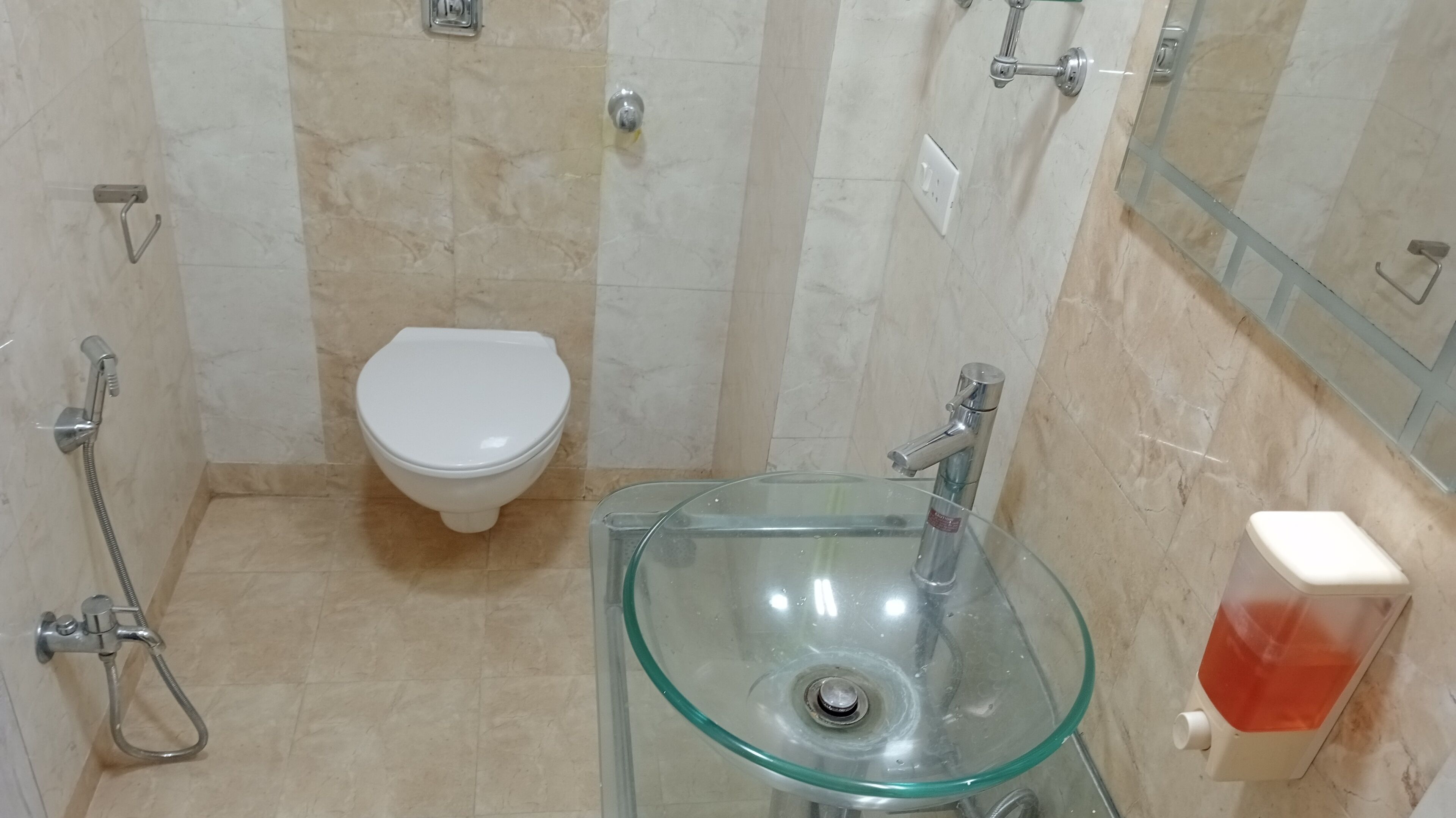 A bathroom with a toilet, a glass sink, and a handheld showerhead.