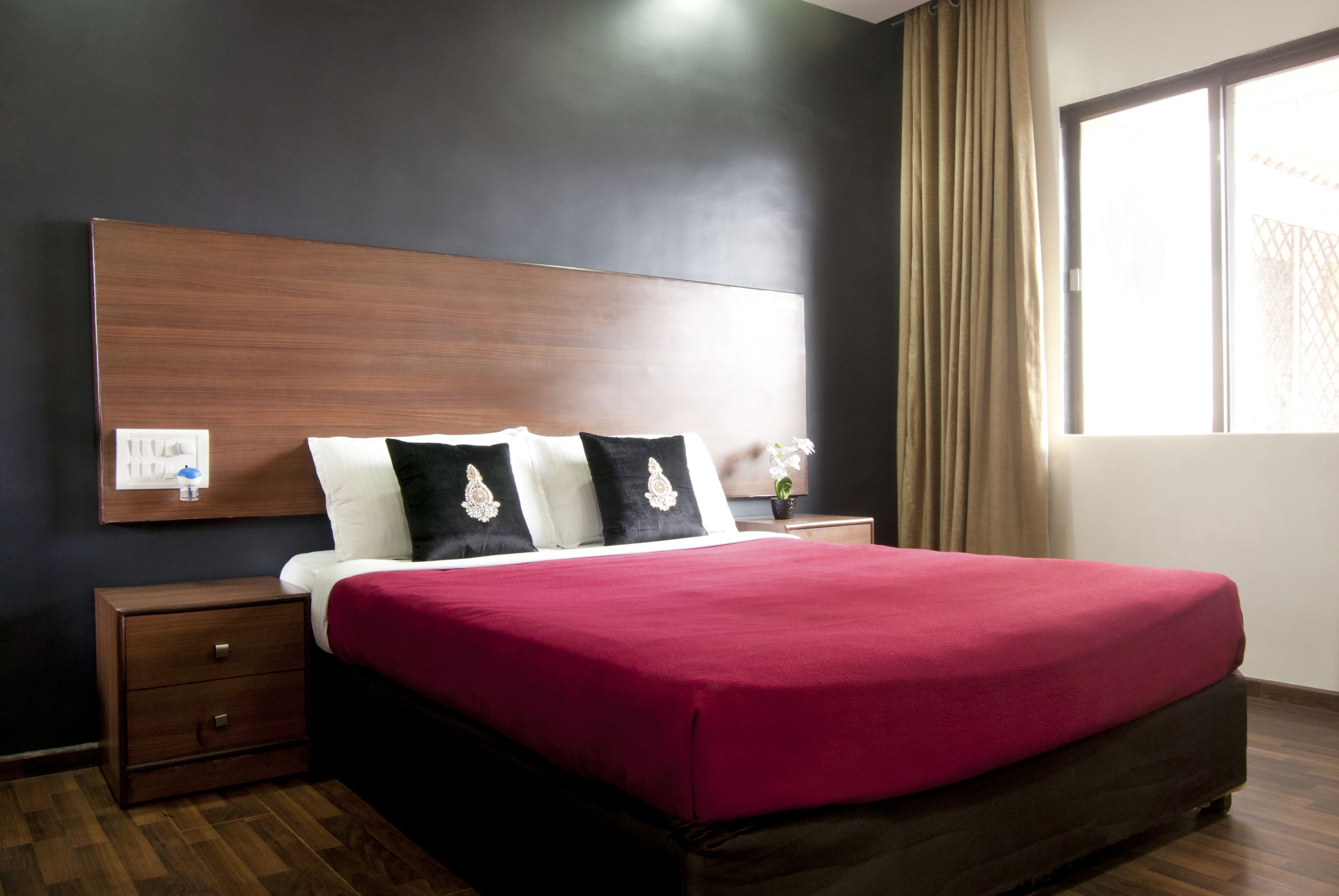 A hotel room with a large bed, a wooden headboard, a nightstand, and a window with curtains.
