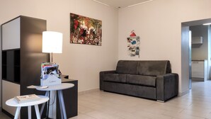 A modern living room with a grey sofa, a small round table with a lamp, and a wall-mounted magazine rack. - Le Puy Carmin - Gîte (Bazoges-en-Paillers)