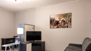 A modern living room with a flat-screen TV, a dark-colored sofa, and a painting on the wall. - Le Puy Carmin - Gîte (Bazoges-en-Paillers)
