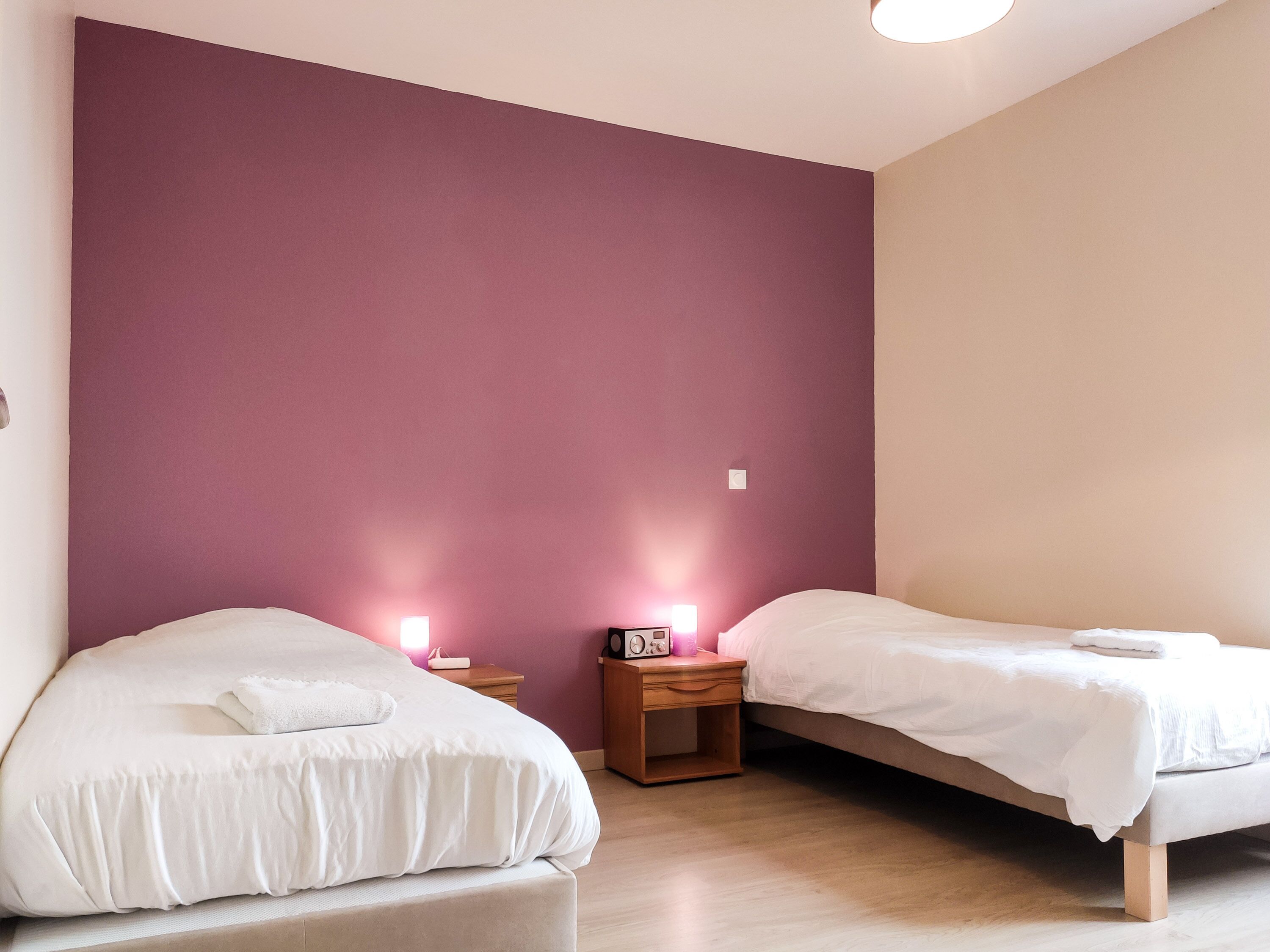 A bedroom with two beds, a nightstand with a radio, and a wall with a purple accent.