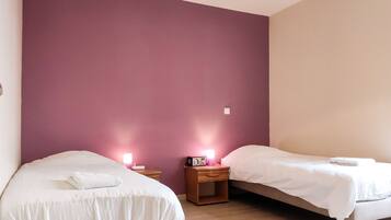 A bedroom with two beds, a nightstand with a radio, and a wall with a purple accent.