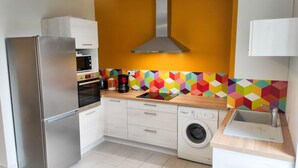 A compact kitchen with a stainless steel refrigerator, built-in oven, microwave, coffee maker, and a washing machine. - Le Puy Carmin - Gîte (Bazoges-en-Paillers)