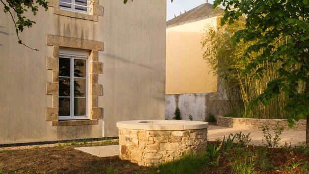 A stone fountain in a garden with a building in the background. - Le Puy Carmin - Gîte (Bazoges-en-Paillers)