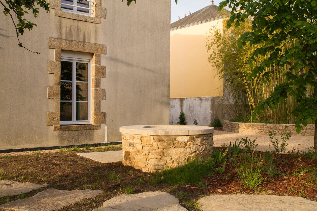 A stone fountain in a garden with a building in the background.