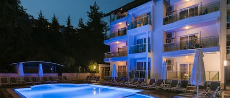A multi-story hotel with a swimming pool, lounge chairs, and umbrellas.