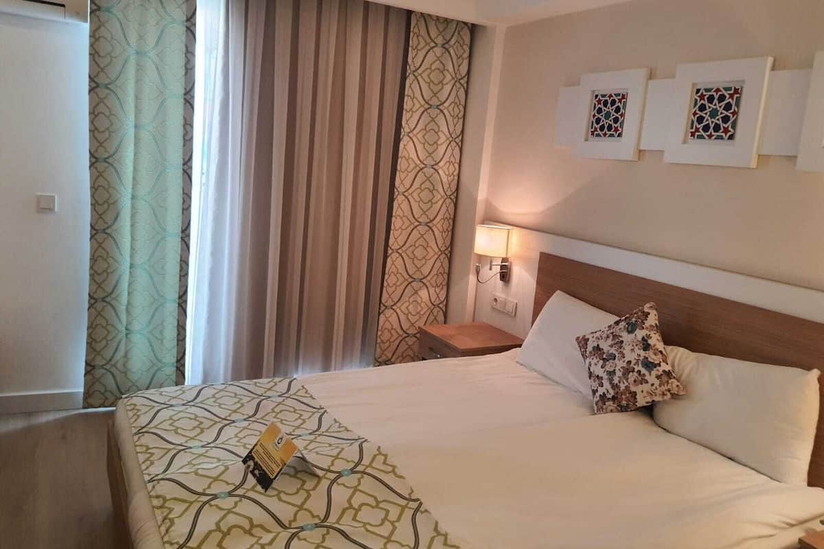 A hotel room with a bed, curtains, a nightstand, a lamp, and wall art.