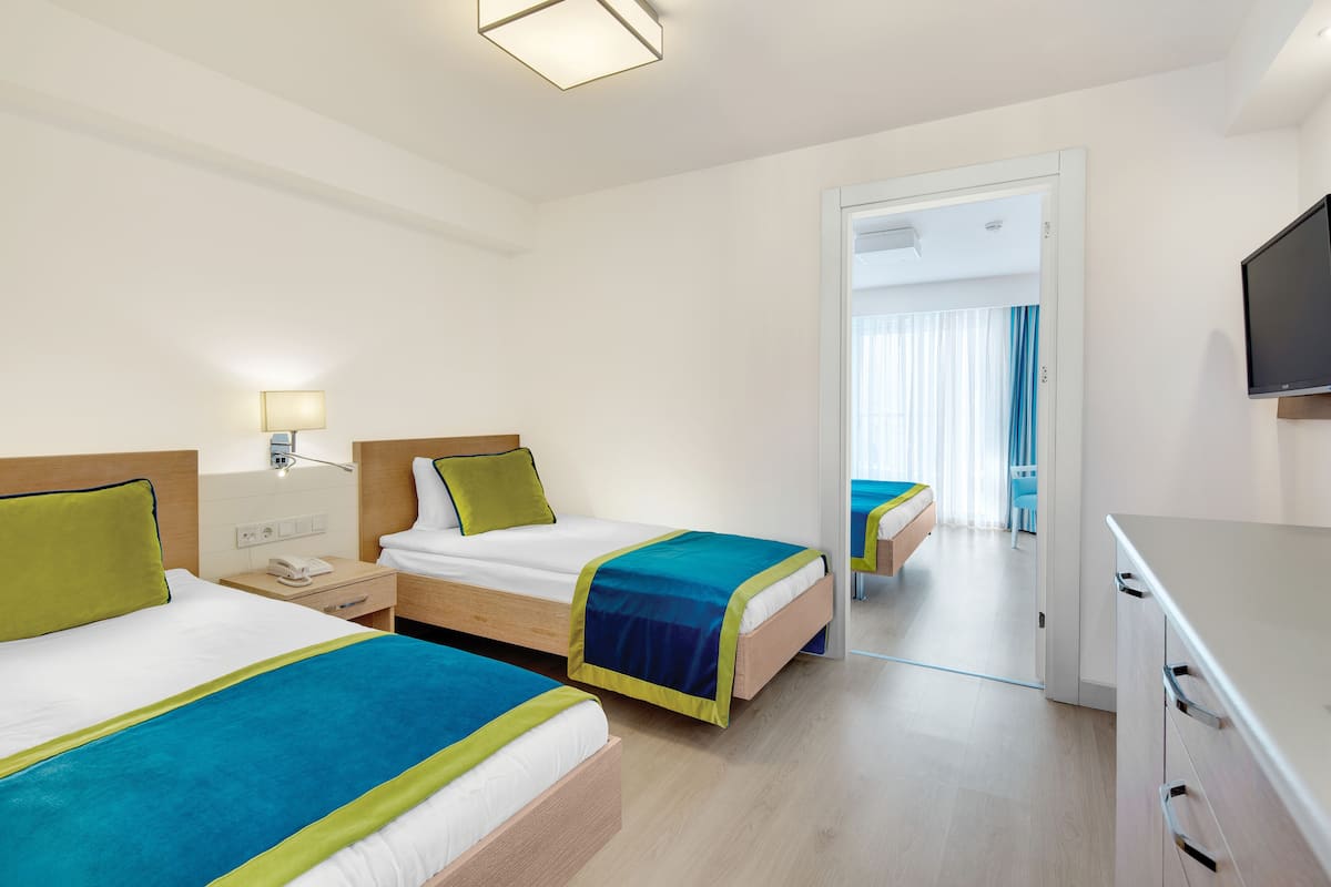 A hotel room with two beds, a desk, a chair, and a TV.