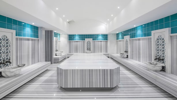 Un baño moderno con un lavamanos grande en el centro, varios espejos en la tocador y suelo de baldosas.
