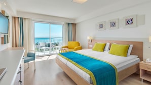Habitación de hotel con una cama grande, un escritorio, una silla y un balcón con vistas al mar.