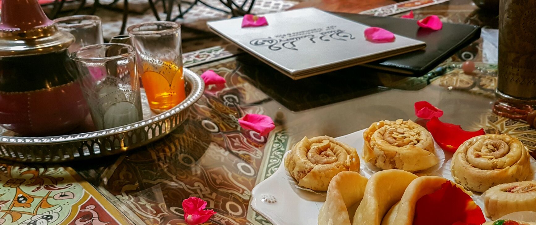 A table with a tray of pastries, glasses of tea, and a teapot.