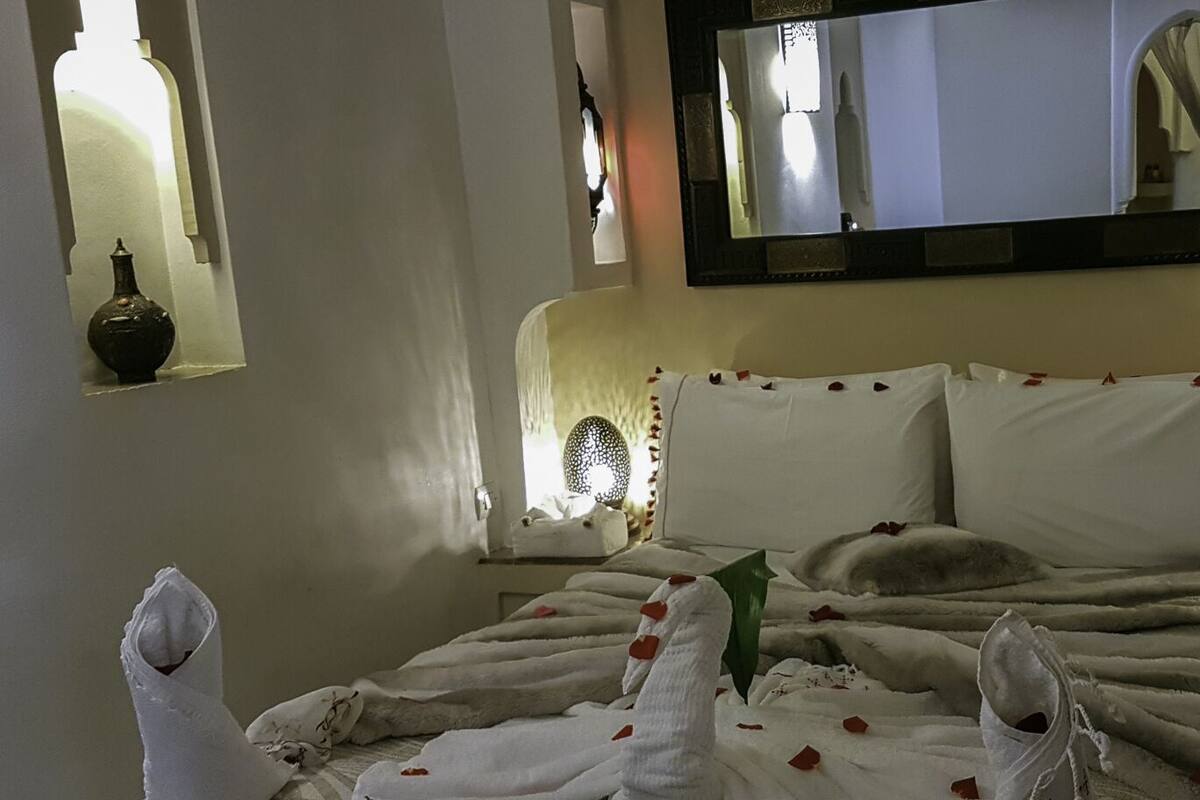 Una habitación de hotel con una cama, una mesita de noche, un espejo y una ventana con una lámpara decorativa.