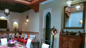 Una habitación con un sofá rojo, una mesa de comedor con un centro de mesa floral y un aparador de madera con un espejo.