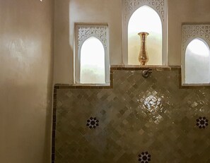 Un baño con pared de azulejos, un jarrón decorativo y tres ventanas de arco.