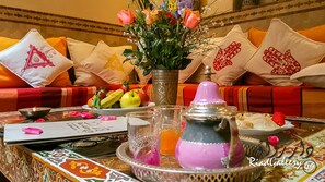 Un ambiente tradicional marroquí con un sofá, almohadones, una bandeja con comida, una tetera y un florero.