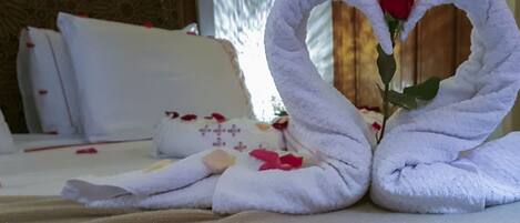 A bed with white linens and a heart-shaped towel arrangement.