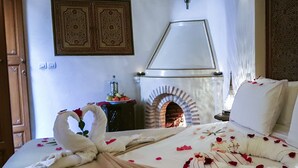 Habitación de hotel con una cama decorada con pétalos de rosa y una toalla con forma de cisne, chimenea y dos paneles decorativos en la pared.
