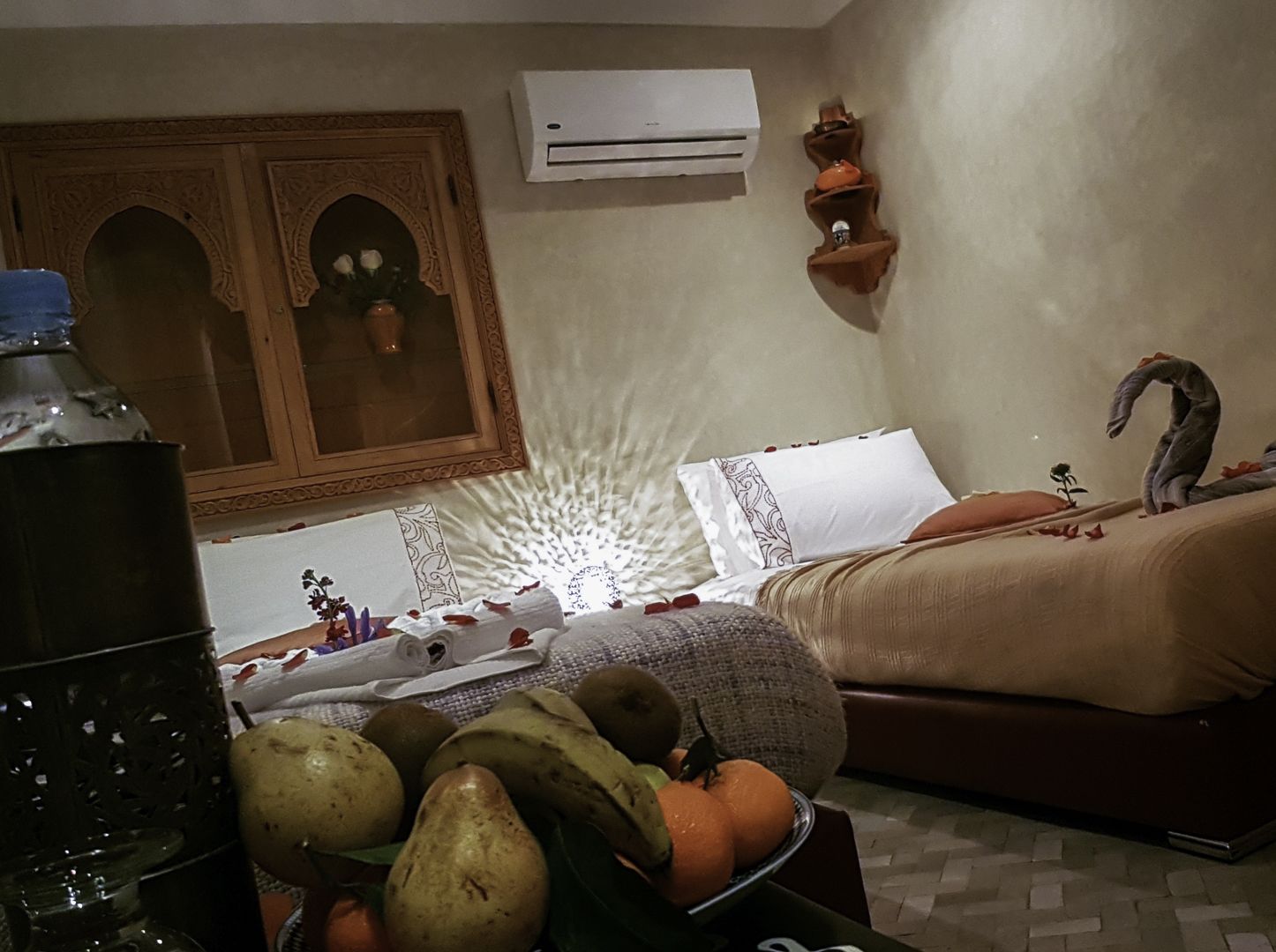 A bedroom with a bed, pillows, a decorative wall, an air conditioner, and a small shelf with items.