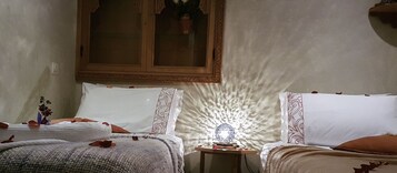 Quarto com duas camas, uma mesinha com abajur e uma janela com moldura decorativa.