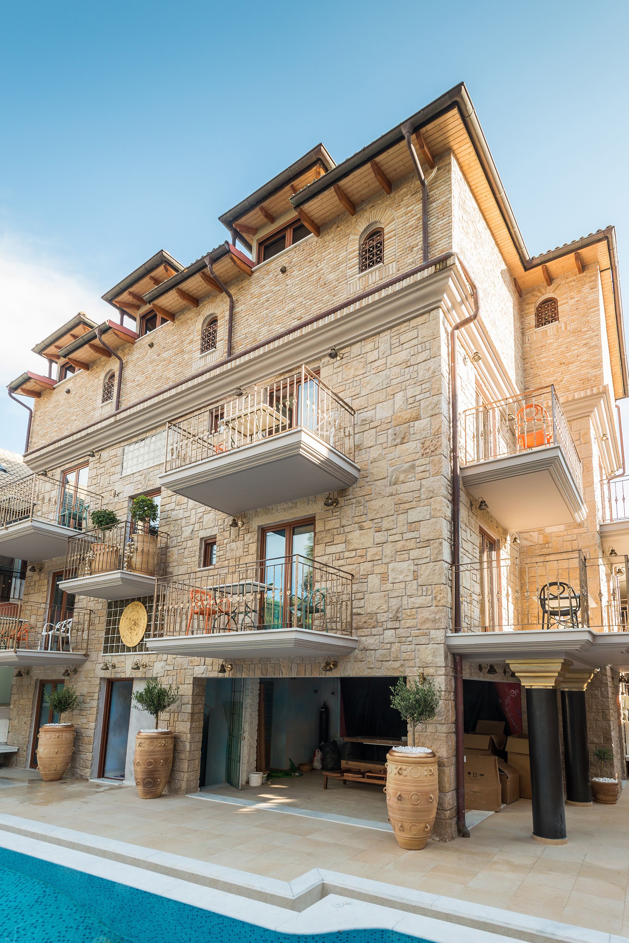 A multi-story stone building with balconies, a swimming pool, and potted plants.