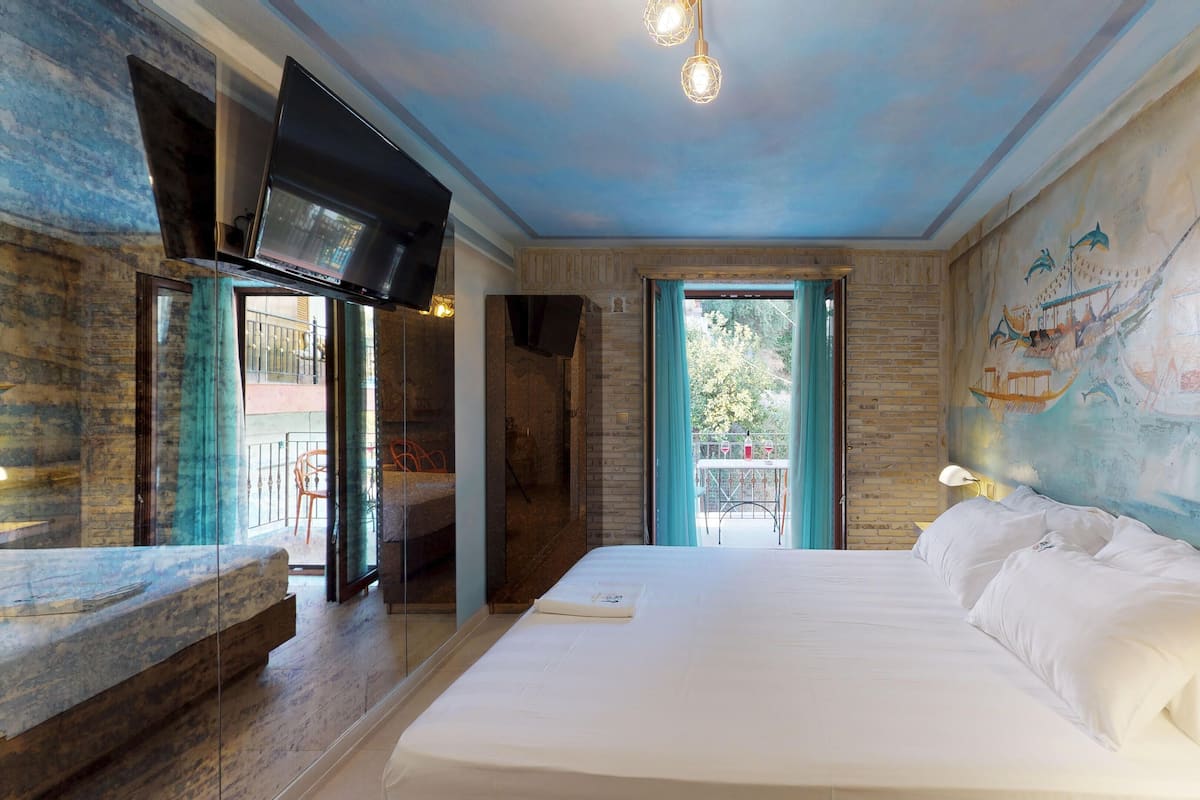 A bedroom with a large bed, a TV mounted on the wall, and a mural of boats on the wall.