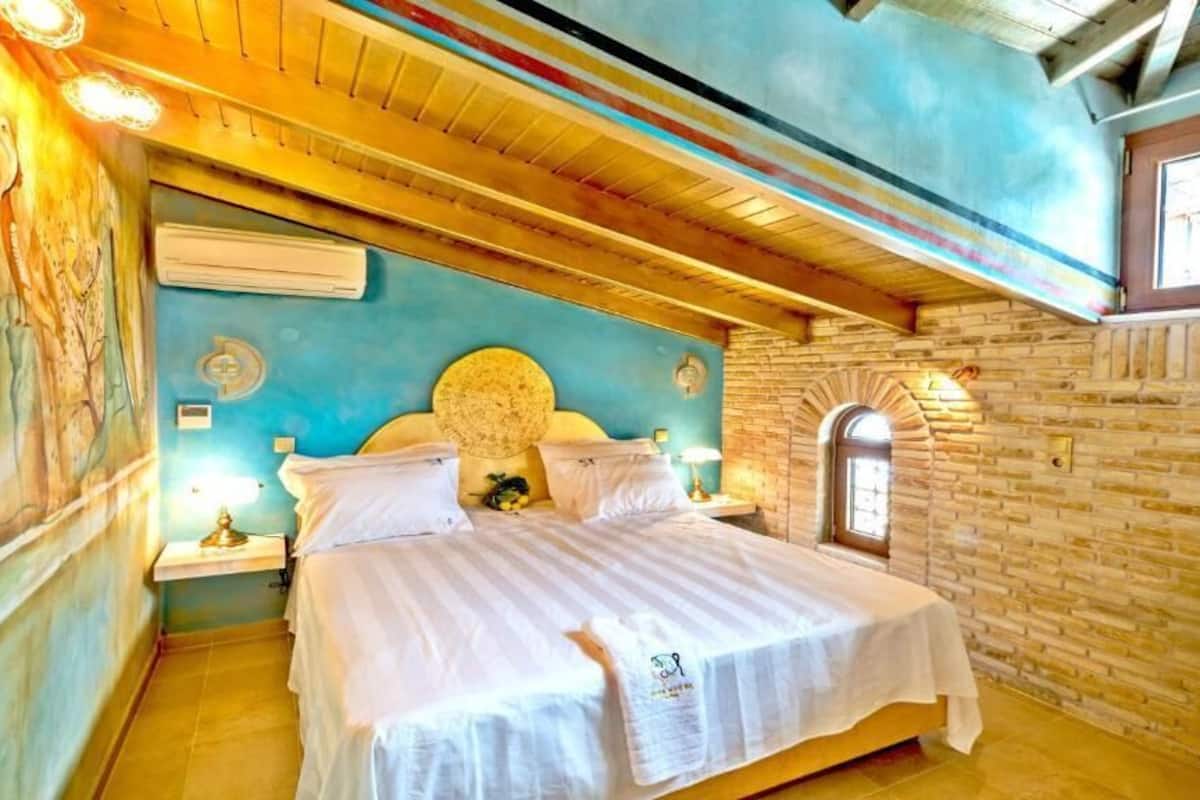 A room with a bed, a wall mural, a window, and a brick wall.
