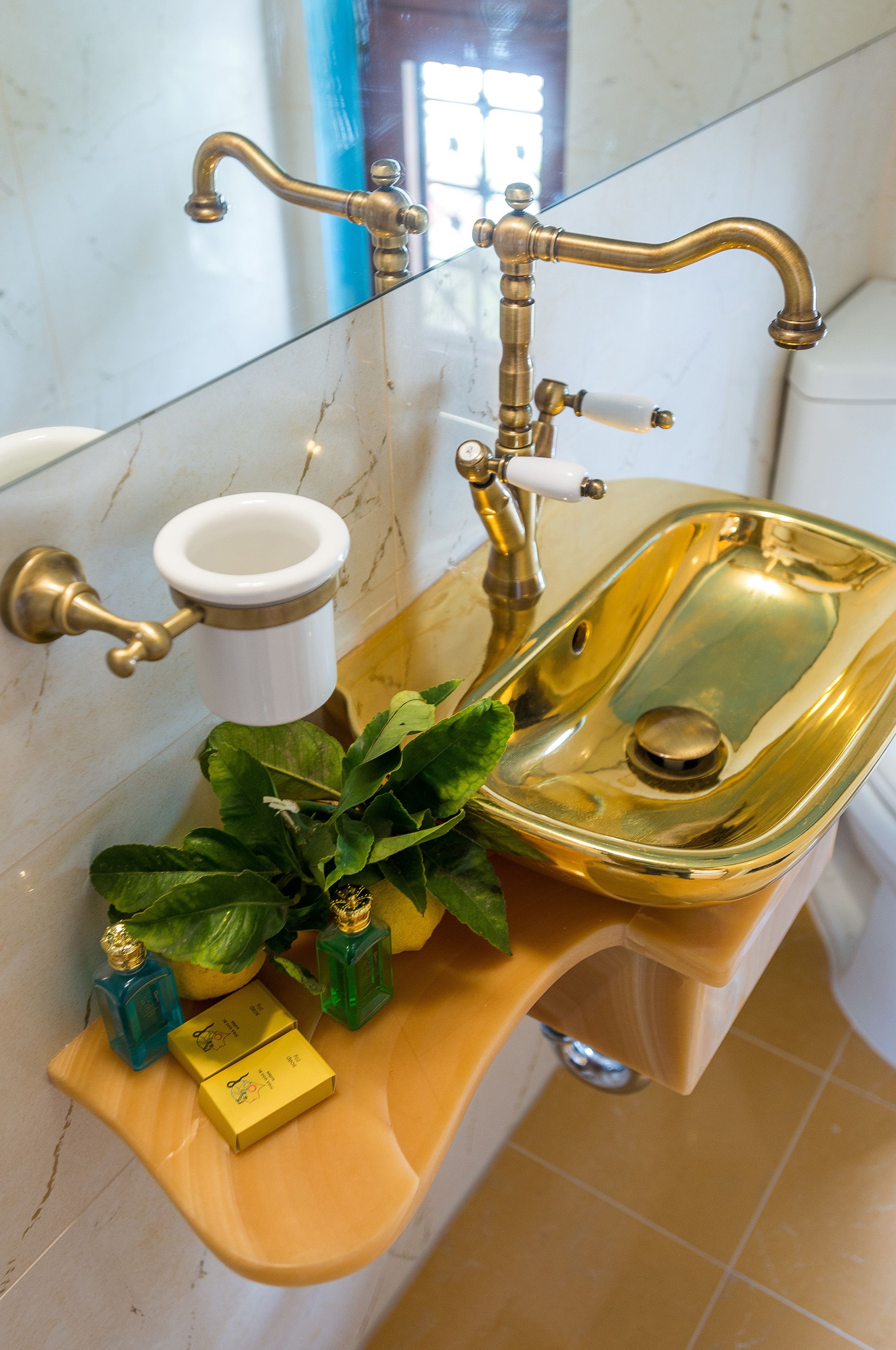 A bathroom with a gold sink, a white toilet, and a mirror.