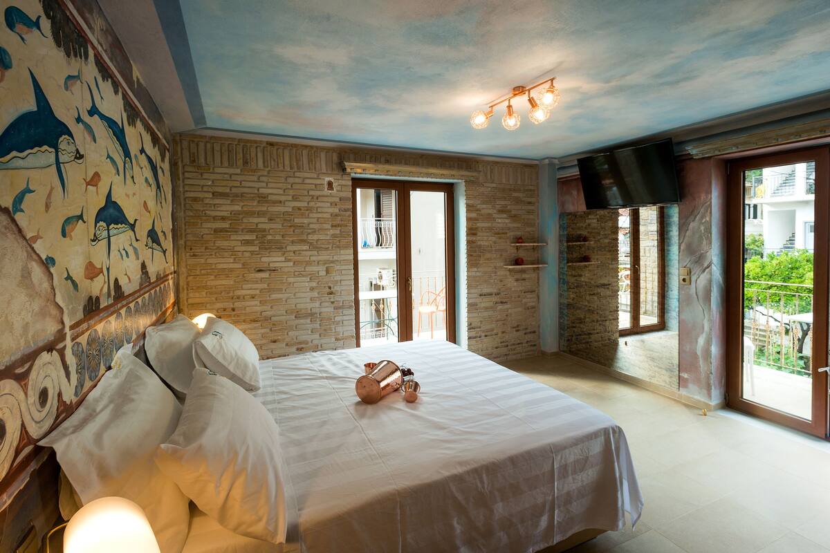 A bedroom with a bed, a mural, a brick wall, a television, and a balcony.
