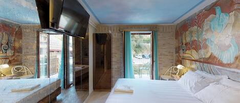 A hotel room with a large bed, a TV mounted on the wall, a balcony with a view, and a mural on the wall.