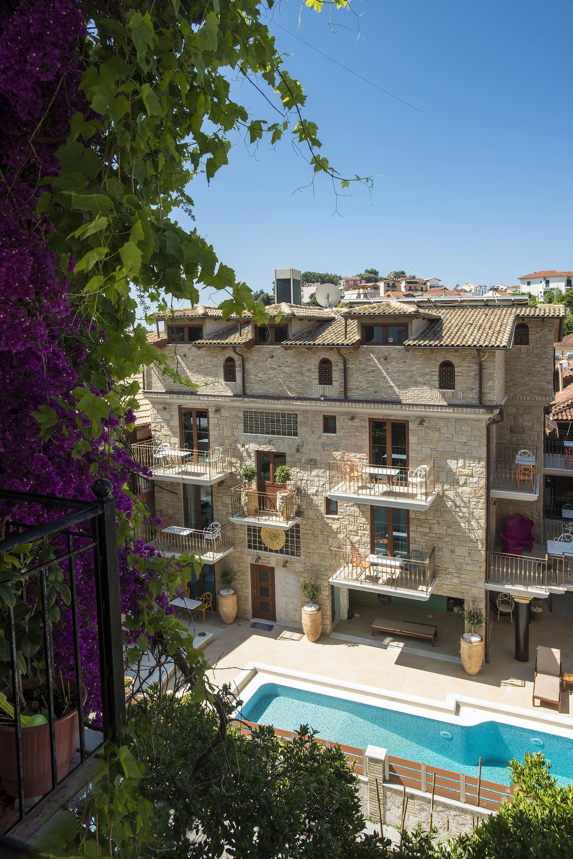 A stone building with multiple balconies, a swimming pool, and potted plants.