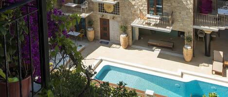 A stone building with multiple balconies, a swimming pool, and potted plants.