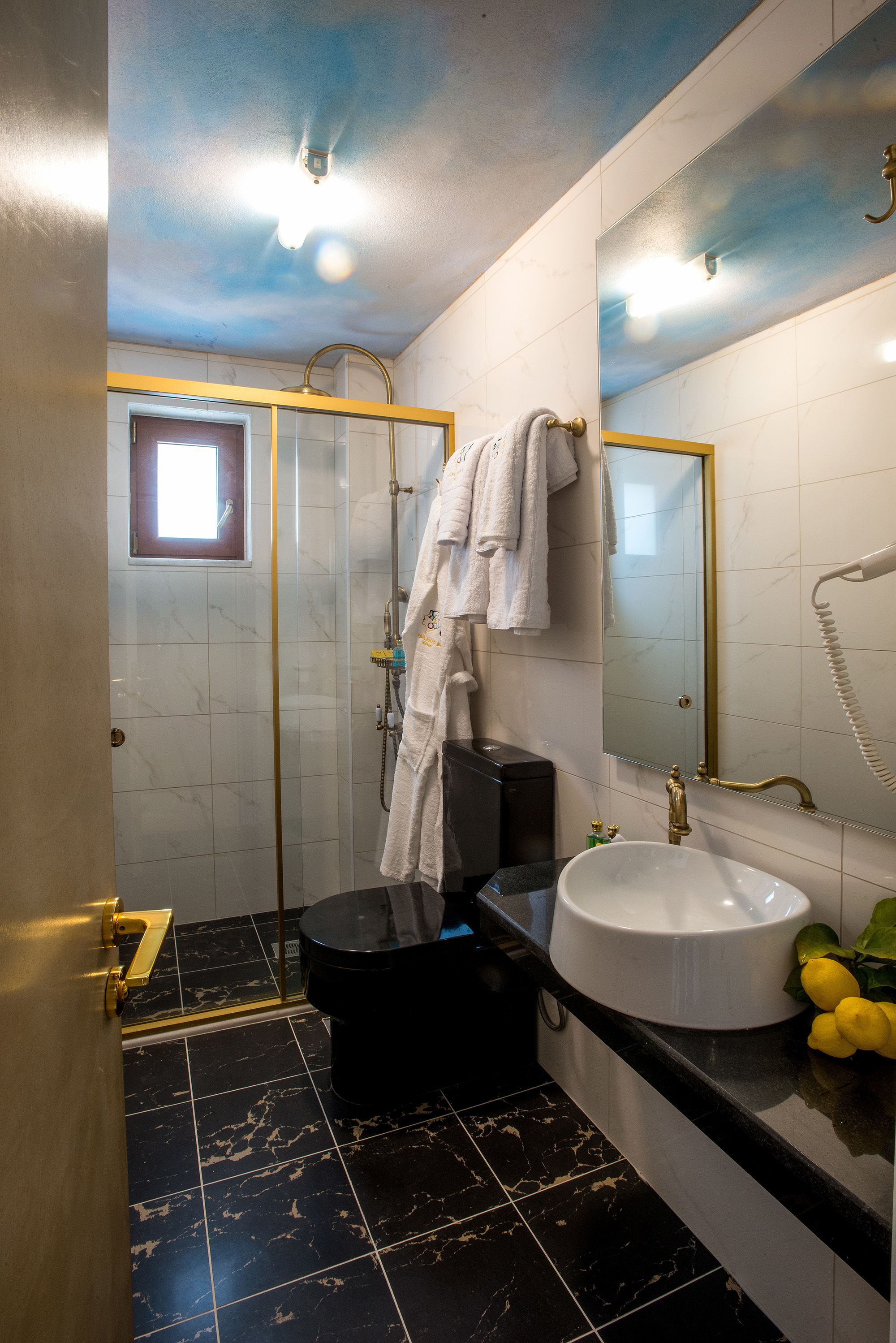 A bathroom with a black and white tiled floor, a white sink, a black toilet, a glass shower enclosure, and a large mirror with a gold frame.